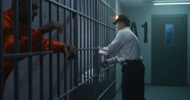 Prison employee brings new prisoner in jail cell Warden brings new prisoner in jail cell and takes off his handcuffs. African American criminals serve imprisonment term in correctional facility or detention center. Guilty murderers in prison cells. prison guard stock pictures, royalty-free photos & images