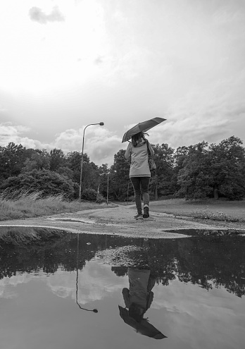 Woman with umbrella walking on wet road against sky