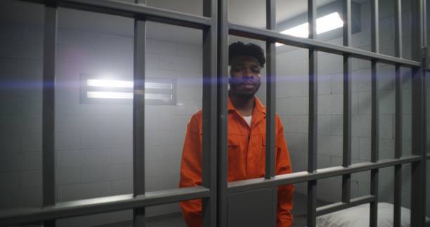 istock Man leans on prison cell bars and looks at camera 1608655272