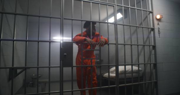 istock Prisoner in orange uniform leans on jail cell bars 1608656276