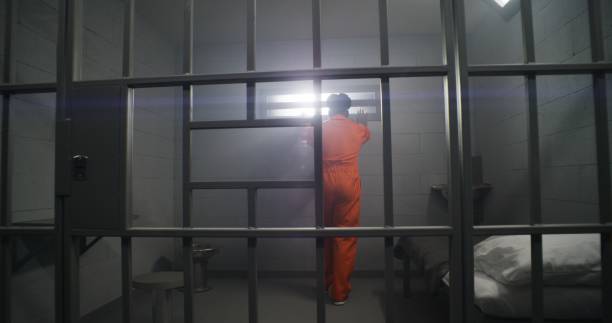 więzień w pomarańczowym mundurze patrzy na zakratowane okno - cela zdjęcia i obrazy z banku zdjęć