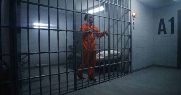 istock Prisoner in orange uniform leans on jail cell bars 1608657804