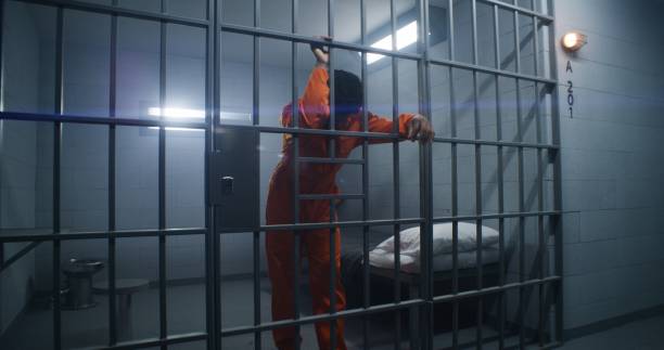 istock Prisoner in orange uniform leans on jail cell bars 1608660956