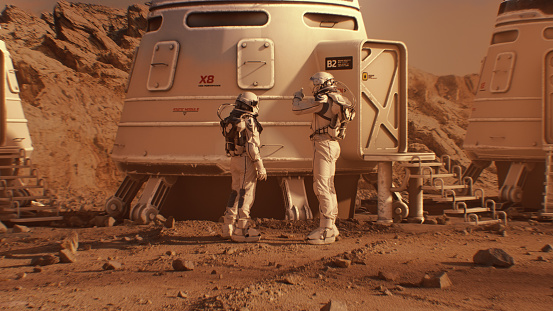 Two astronauts in spacesuits walk toward research station, colony or scientific base on Mars. Manned exploring space mission on red planet. Futuristic colonization and space exploration concept.