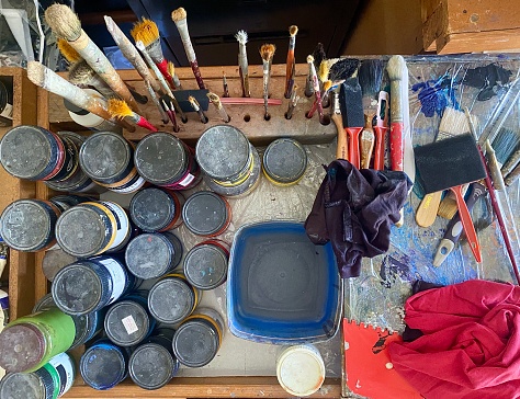 Horizontal flat lay of painting artists table filled with acrylic paints, brushes, sponges, materials and paint equipment seen in creative studio Australia