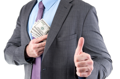 Businessman puts dollars in the inner pocket. Focus is on dollars and hand, while the thumb up is slightly out of focus