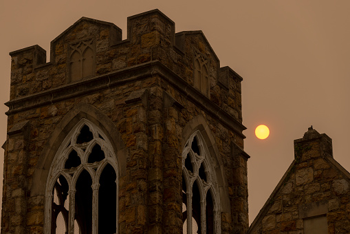 Church cathedral tower in the dark sky is under the smog from Canadian fires in Jim Thorpe (Mauch Chunk) at sunset. Appalachian ountains, Poconos, Pennsylvania. Low angle view