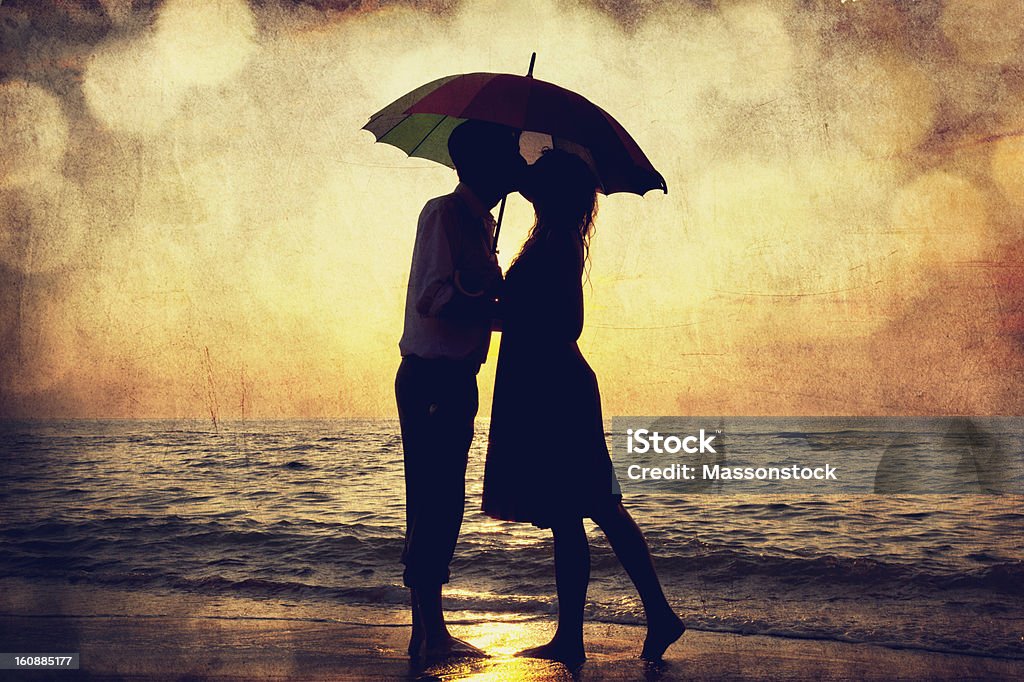 Couple kissing under umbrella at the beach in sunset. Couple kissing under umbrella at the beach in sunset. Photo in old image style. Couple - Relationship Stock Photo