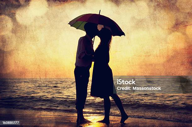 Couple Kissing Under Umbrella At The Beach In Sunset Stock Photo - Download Image Now