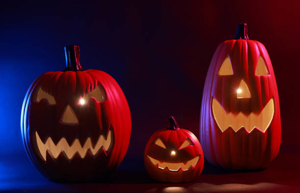 Close-up view of scary Halloween pumpkin with eyes glowing inside a dark colorful background. Halloween pumpkin smile and scary eyes for the party night.