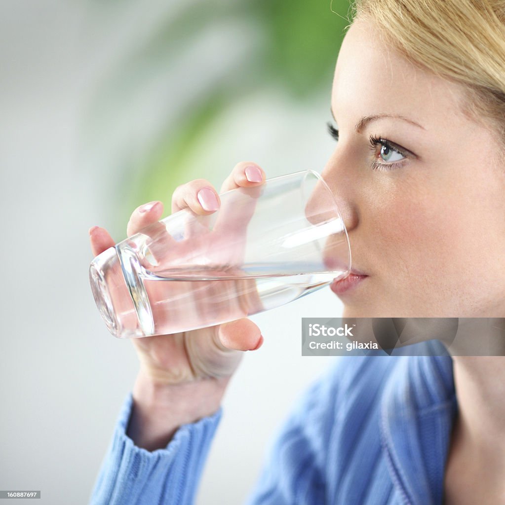Water. Closeup of adult blond woman drinking water.She's holding a glass and looking straight ahead. Her hair is tied with a clip and she's wearing blue sweater 20-24 Years Stock Photo