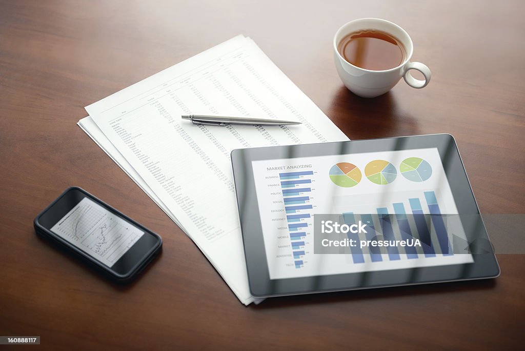 Modern business workplace Modern workplace with digital tablet and mobile phone, pen and papers with numbers. Desktop PC Stock Photo