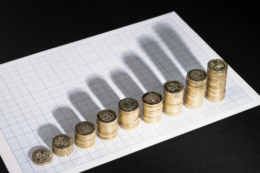 Rising stacks of UK Pound coins, casting shadows onto graph paper.