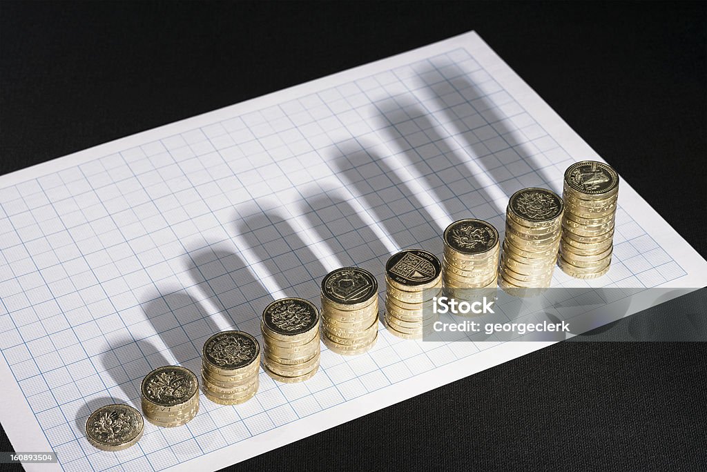 Analysis of Growth Rising stacks of UK Pound coins, casting shadows onto graph paper. Investment Stock Photo