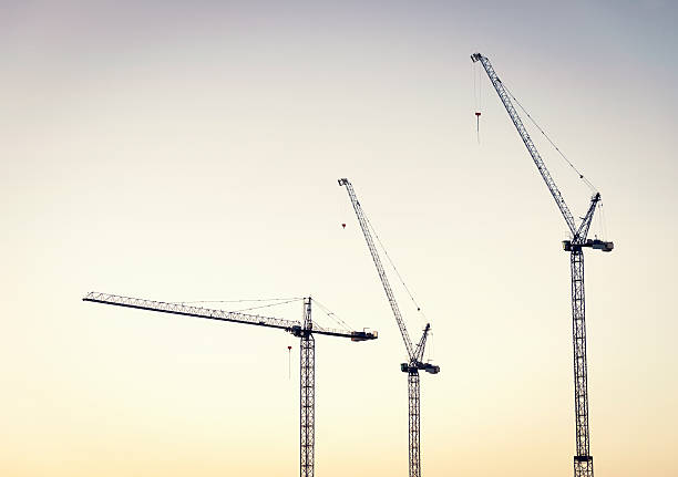 Construction Cranes at Dawn Three large construction cranes at a large industrial building site, photographed at dawn. crane machinery stock pictures, royalty-free photos & images