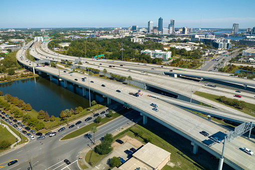 Aerial view of Jacksonville city with high office buildings and american freeway intersection with fast driving cars and trucks. View from above of USA transportation infrastructure.