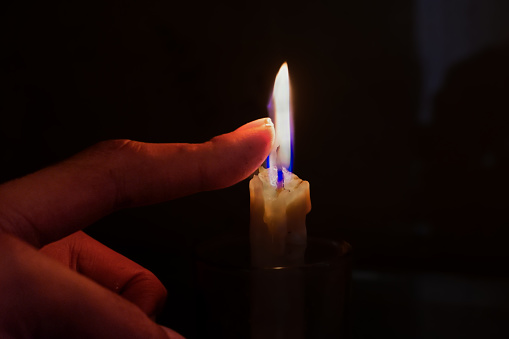 The fingertips of a hand that touches the flame of a lit candle.