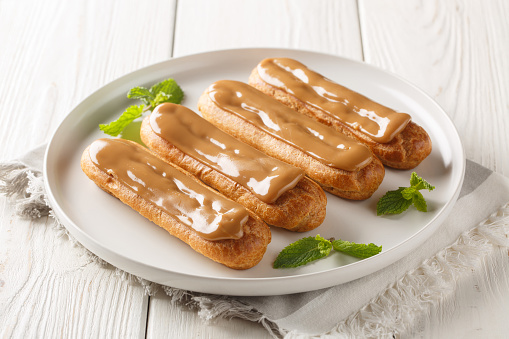 Exquisite eclairs with creamy filling and topped with soft delicate caramel close-up in a plate on the table. Horizontal