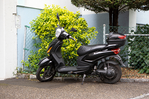 Moped parked by a green bush outside an apartment building