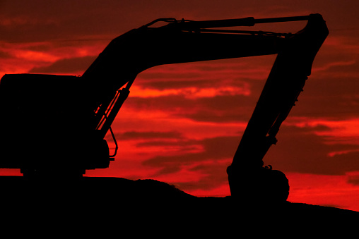 Silhuette of a digger with construction worker. Photo taken during sunset, with giant sun in the background.
