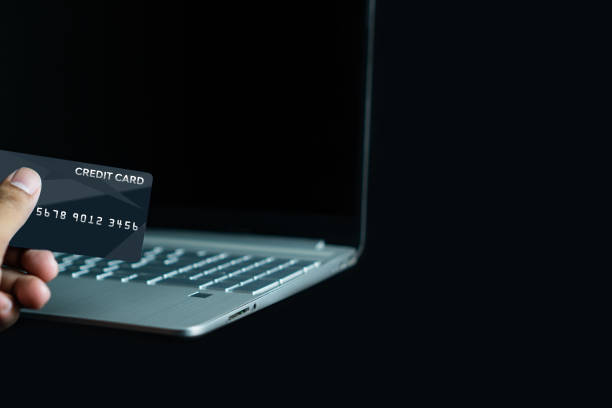istock Hand holding credit card and using laptop computer for online shopping on black background 1609058355