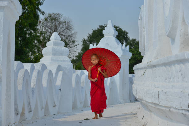 A Buddhist novice monk with a red umbrella walking at the white temple.