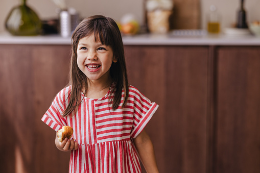 A smiling adorable Japanese child enjoying some tasty food while standing in the kitchen.