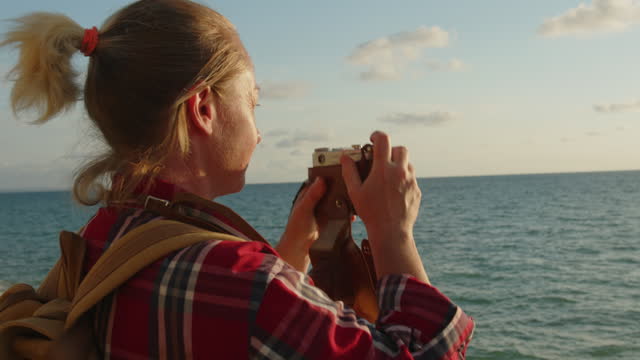 Woman tourist photographer takes pictures on retro camera from viewpoint on sea coast.