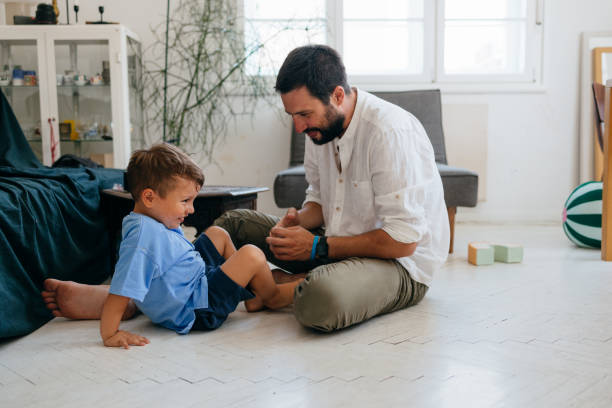 istock Happy Young Father Sitting on the Floor and Playing with his Son 1609207122