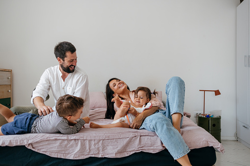 Smiling parents lying on the bed with their two toddlers, son and daughter.