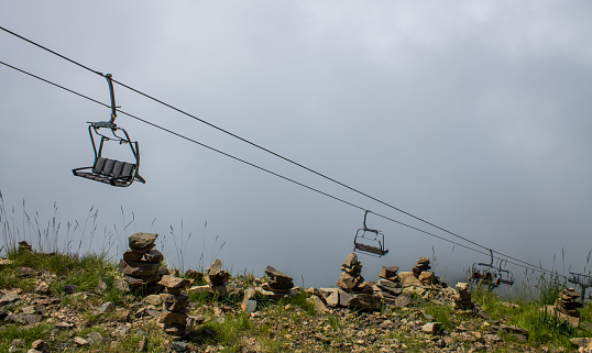 Metal chairs of the cable car move on the hillside against the backdrop of a large dramatic cloud and stone pyramids on Krasnaya Polyana in Russia and a space for copy. Concept - travel
