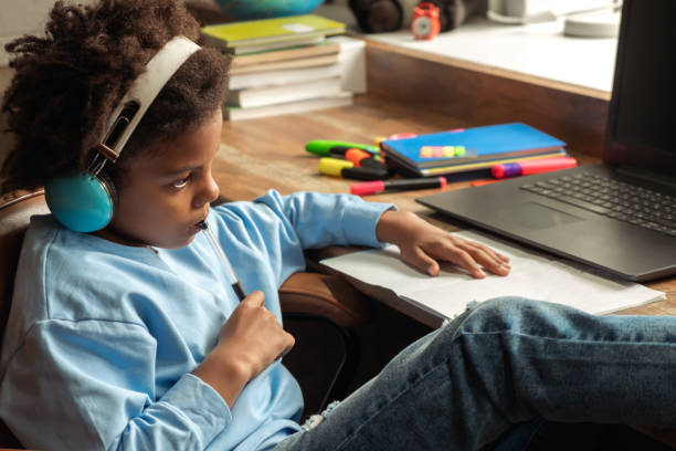 istock African-American girl doing homework,making notes,using headphones and laptop at home.Back to school concept.School distance education at home,home schooling,e-learning,diverse people 1609223728