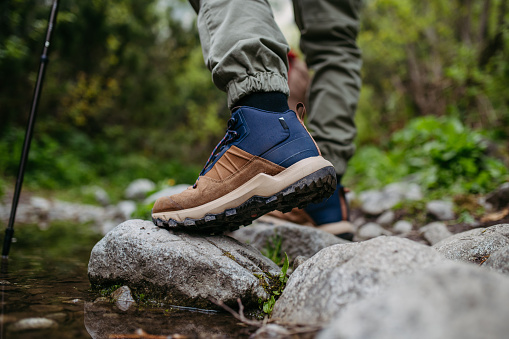 Close-up of hiking shoe stepping on rock. Hiking boots providing better support and stability on hiking trail. The hiker shown in motion, with one foot planted on the mountain rock.
