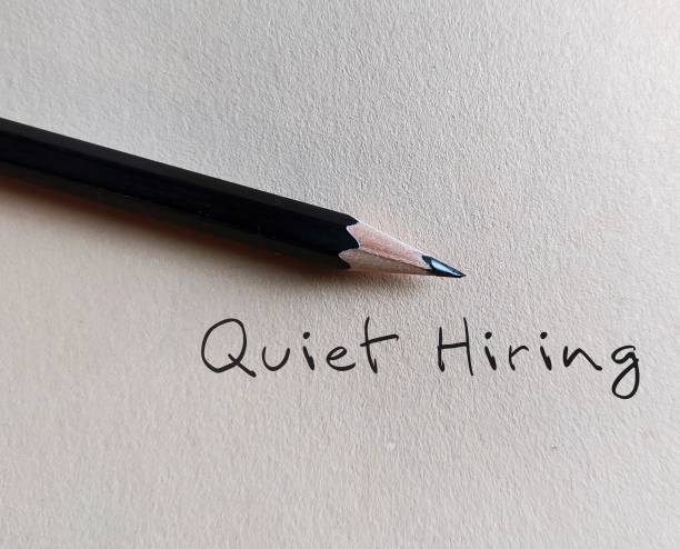 istock Pencil writing on beige background with handwritten text QUIET HIRING - HR buzz word of recruiting strategy, employees who stand out by going above and beyond get more attention, money, praise, and more opportunities 1609335291