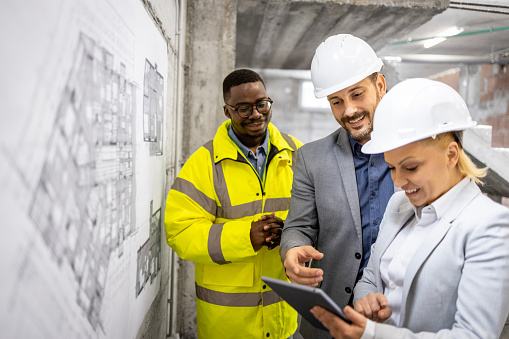 Team of construction engineers working together on building site and discussing project plan or blueprint.