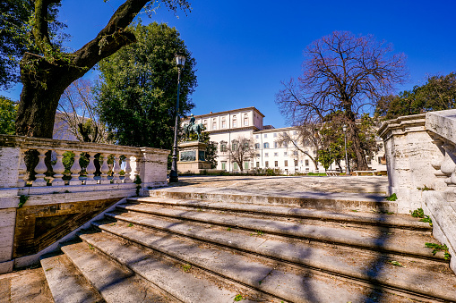 A glimpse of the Palazzo del Quirinale (Quirinal Palace) in the historic heart of Rome seen from the gardens of the Carlo Alberto public park. On the left, the bronze equestrian statue of King Carlo Alberto of Savoy, created in 1899 by the sculptor Raffaello Romanelli. The Quirinal Palace is currently the official seat of the President of the Italian Republic, elected every seven years by the Italian Parliament. Built in neoclassical style on the Quirinal hill between 1573 and 1583 as the summer residence of Pope Gregory XIII, this palace over the centuries has been the residence of the Popes (1605-1870), the residence of the King of Italy (1871-1946) and official seat of the Presidency of the Republic (from 1946 to today). Some of the most important Italian architects and artists participated in its construction and decoration, including Gian Lorenzo Bernini, Carlo Maderno, Guido Reni and Domenico Fontana. The Quirinal Palace, with an extension of 110,000 square meters, is the sixth largest building in the world. In 1980 the historic center of Rome was declared a World Heritage Site by Unesco. Super wide angle image in high definition quality.