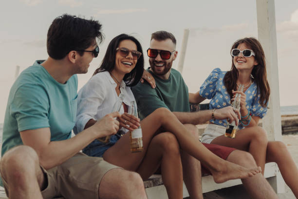 istock Group of young people talking and smiling while enjoying cold beer on the beach together 1609409404