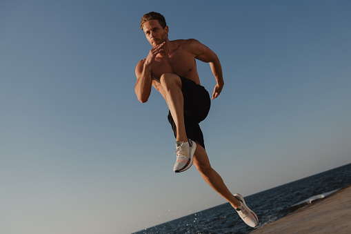 Confident muscular man jumping outdoors with the sea on a background