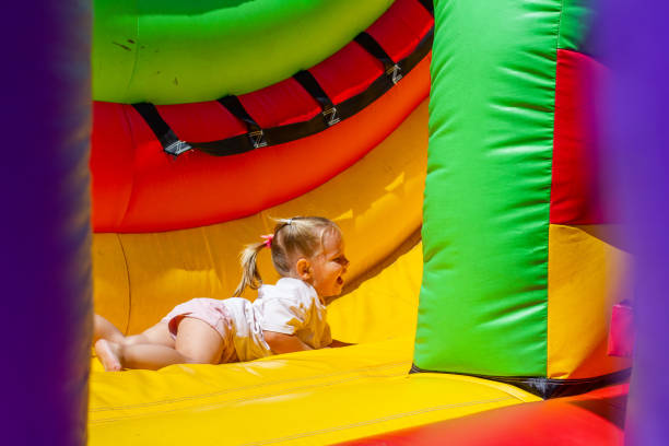 istock Smiling and laughing, a child girl slides down an inflatable multi-colored trampoline slide. The child has fun in the summer park on a sunny hot day. The concept of children in the amusement park. 1609438441