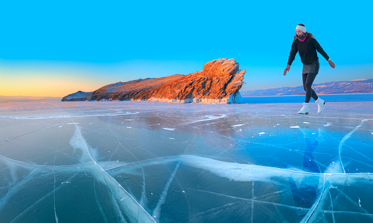 A young happy woman is skating on the transparent ice of the frozen Lake Baikal on a sunny winter day - World-famous figure skater \