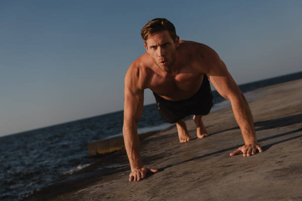 istock Confident young shirtless man doing push-ups while exercising outdoors with the sea on background 1609441228