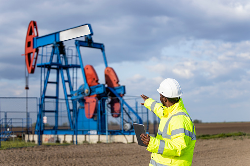 Industrial worker in protective work wear and hard hat monitoring drilling operations of oil rigs.