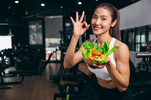 sport healthy beautiful asian woman showing vegetables mix salad for diet food low calories in fitness sport club