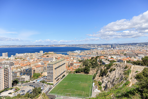 A scenics aerial view of the city of Marseille, bouches-du-rhône, France with a grass football field under a majestic blue sky and some white clouds