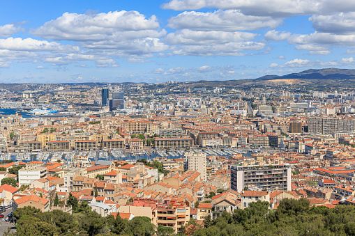 A scenics aerial view of the city of Marseille, bouches-du-rhône, France with the old port (vieux port) in the background under a majestic blue sky and some white clouds