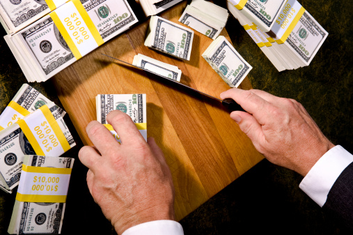 Budget Cutting - A Businessman or Congressman cutting stacks of $100 bills with a Knife and cutting board