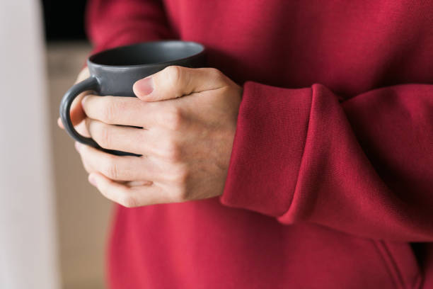 istock Close-up man with cup of coffee. Guy drinks coffee sitting near window 1609523020