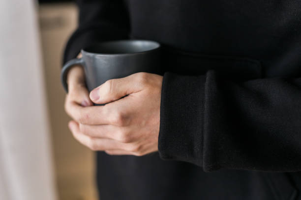 istock Close-up man with cup of coffee. Guy drinks coffee sitting near window 1609528449