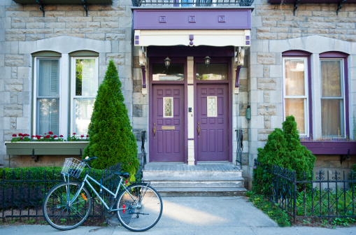 An old style house in the Plateau Mount Royal area in downtown Montreal with purple doors and trim and a bicycle parked in the front on the sidewalk.