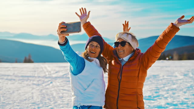 SLO MO A senior woman and her mid-adult daughter have fun as they are taking selfies with a mobile phone in snow
